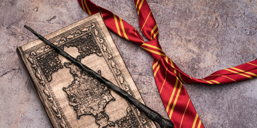 Harry Potter wand, Gryffindor tie, and Hogwarts book on stone backdrop